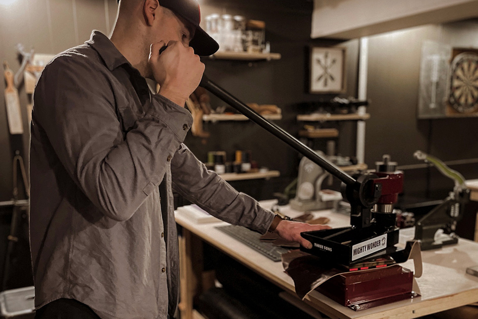 Seth Robinson working with leather press in basement studio (photo courtesy of Three Sons Leather Co.)