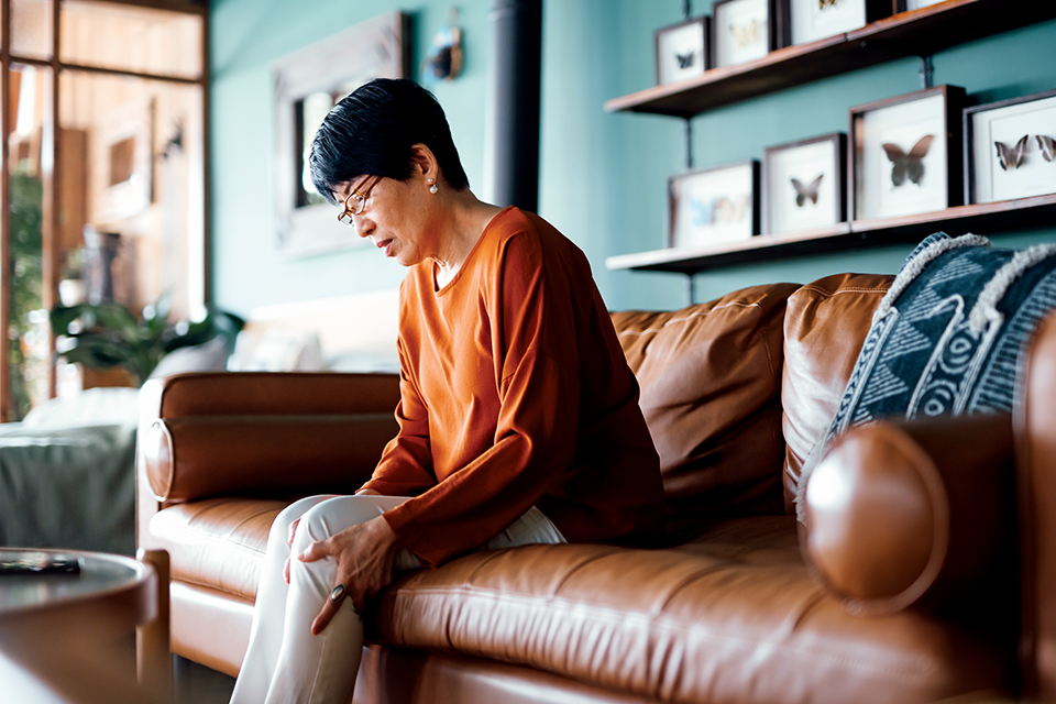 Woman sitting on couch feeling knee (photo by iStock)