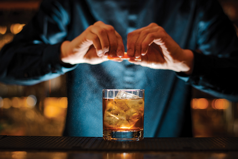 Bartender squeezing orange peel over cocktail (photo by iStock)