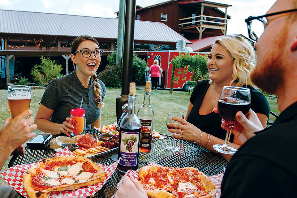 A group of friends share pizza and wine around a patio table. 