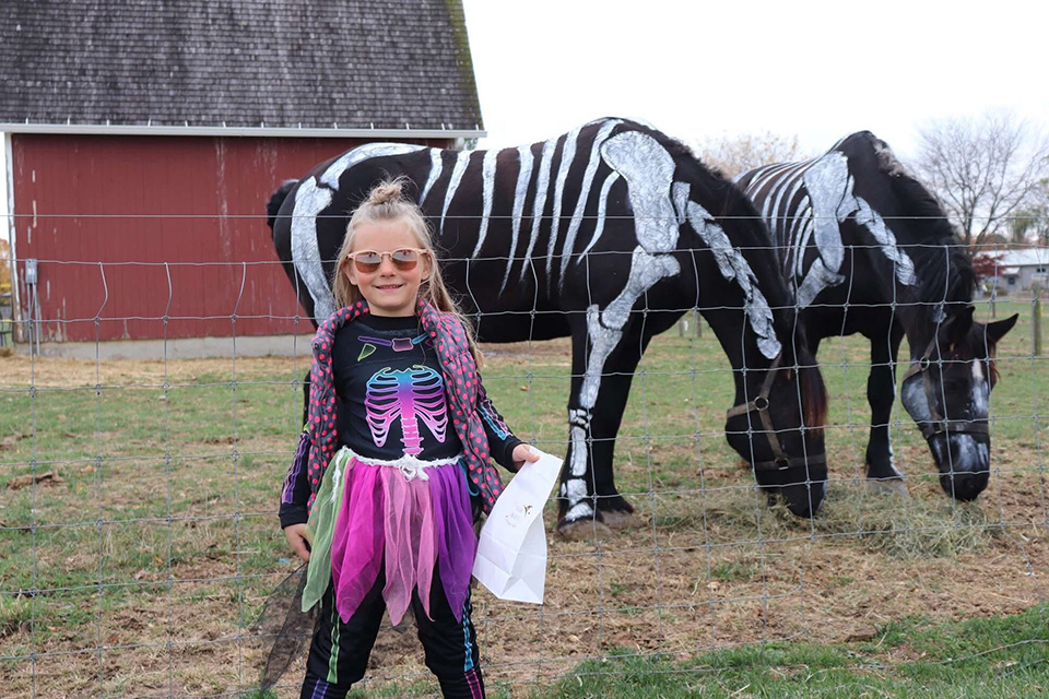 A girl standing by horses during Eerie Nights at Sauder Village in Archbold, Ohio (photo courtesy of Sauder Village)
