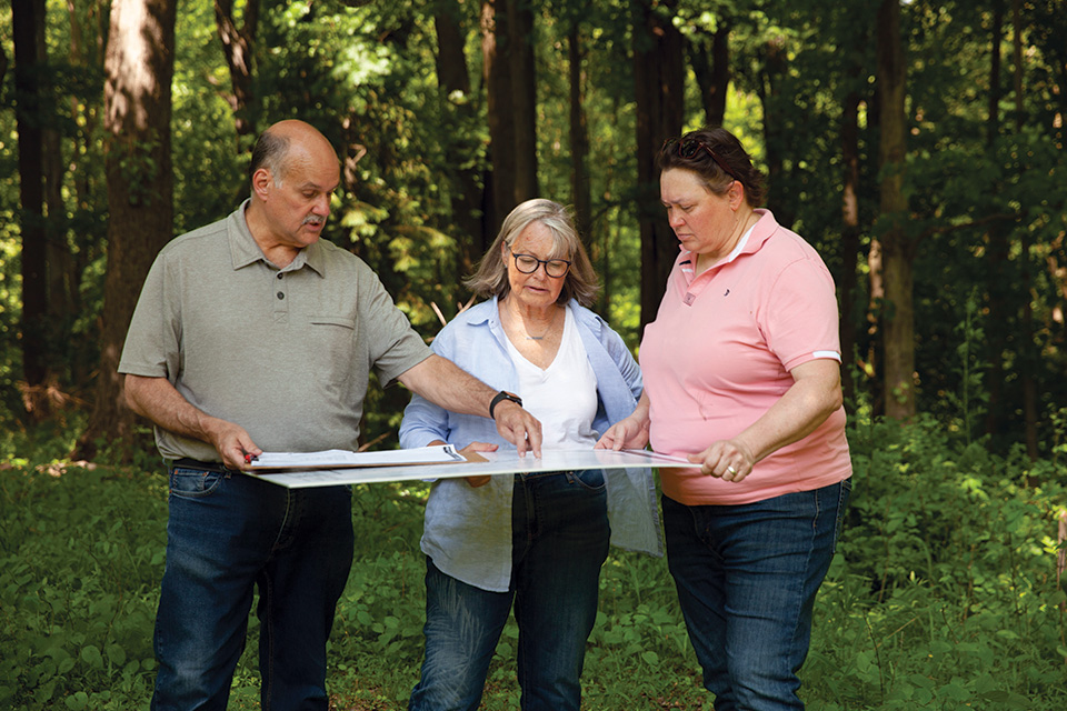 Dave Novak, Debbie Dykstra and Sarah Dykstra looking at RiverRock House site plan (photo © 2024 Warner Bros. Discovery, Inc. or its subsidiaries and affiliates. All rights reserved.)